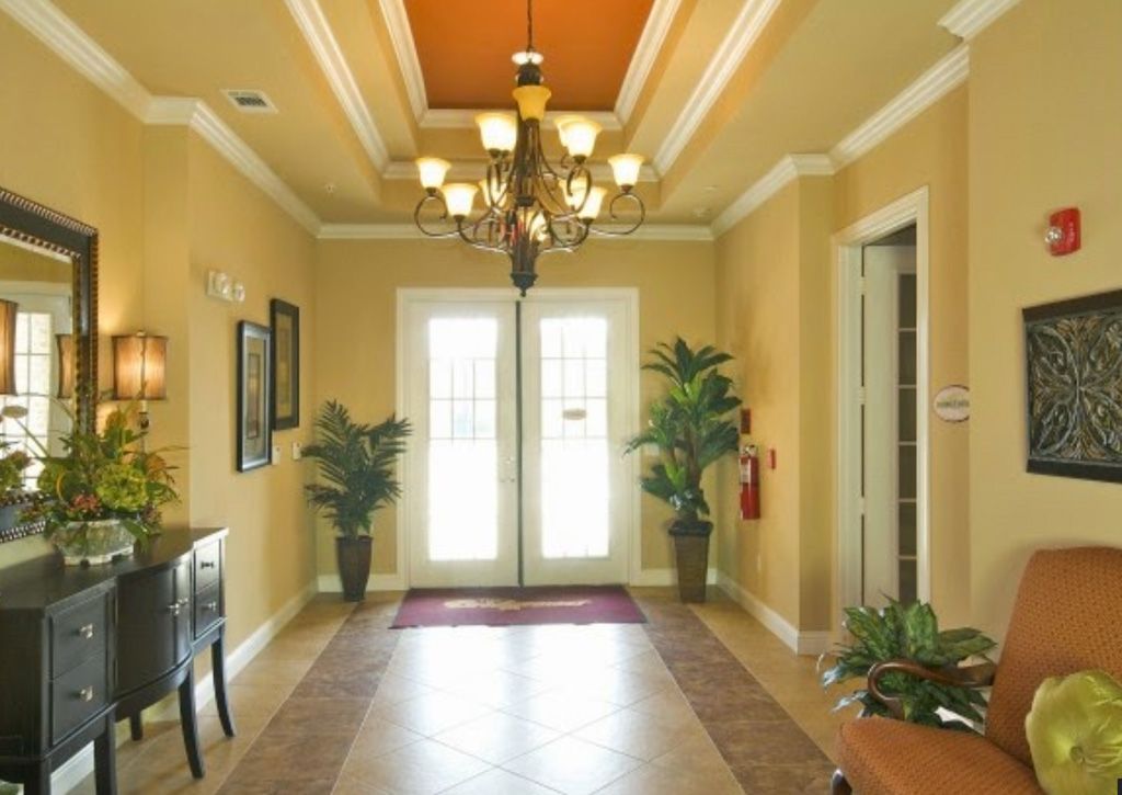 A warmly lit entryway with a chandelier, potted plants, and double French doors.