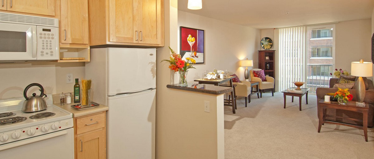 A cozy open floor plan showcasing a kitchen with wooden cabinets and adjacent living area adorned with colorful artwork and furniture.