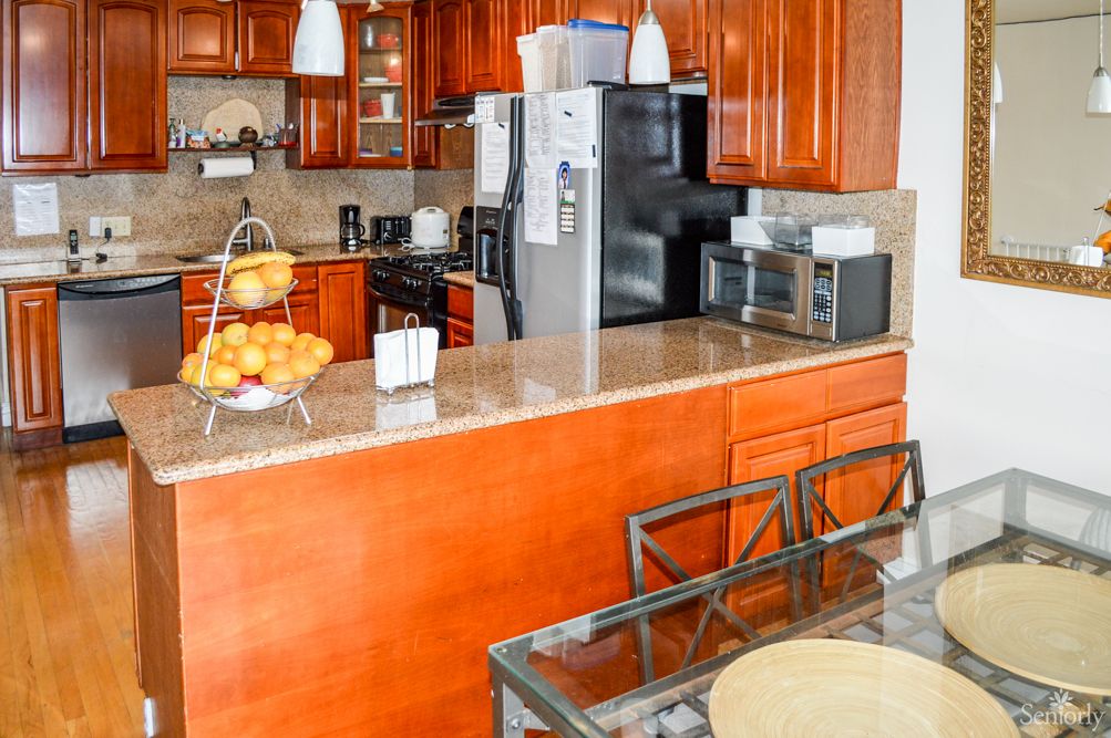 A modern kitchen with wooden cabinets, featuring a countertop with various appliances and seating.