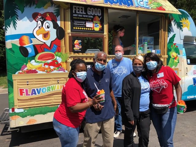 A group of people standing in front of a colorful food truck, all wearing masks.