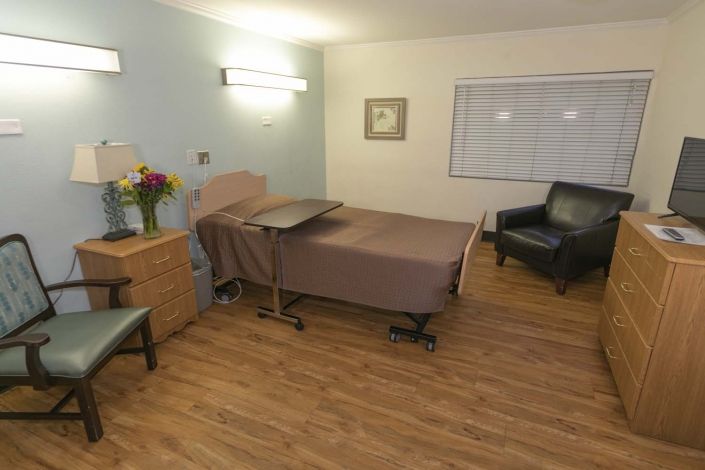 A clean and tidy hospital room with a bed, chairs, and flowers.
