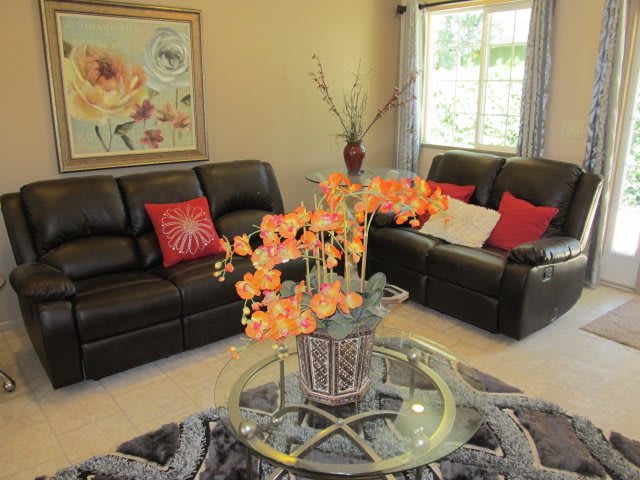 A cozy living room with a floral centerpiece on a glass table surrounded by leather sofas and decorative pillows.