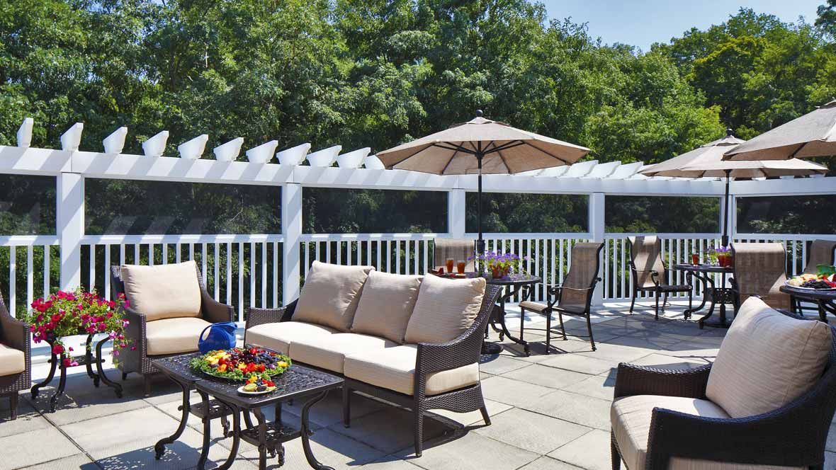 An inviting outdoor patio with comfortable seating and an umbrella, surrounded by lush greenery.