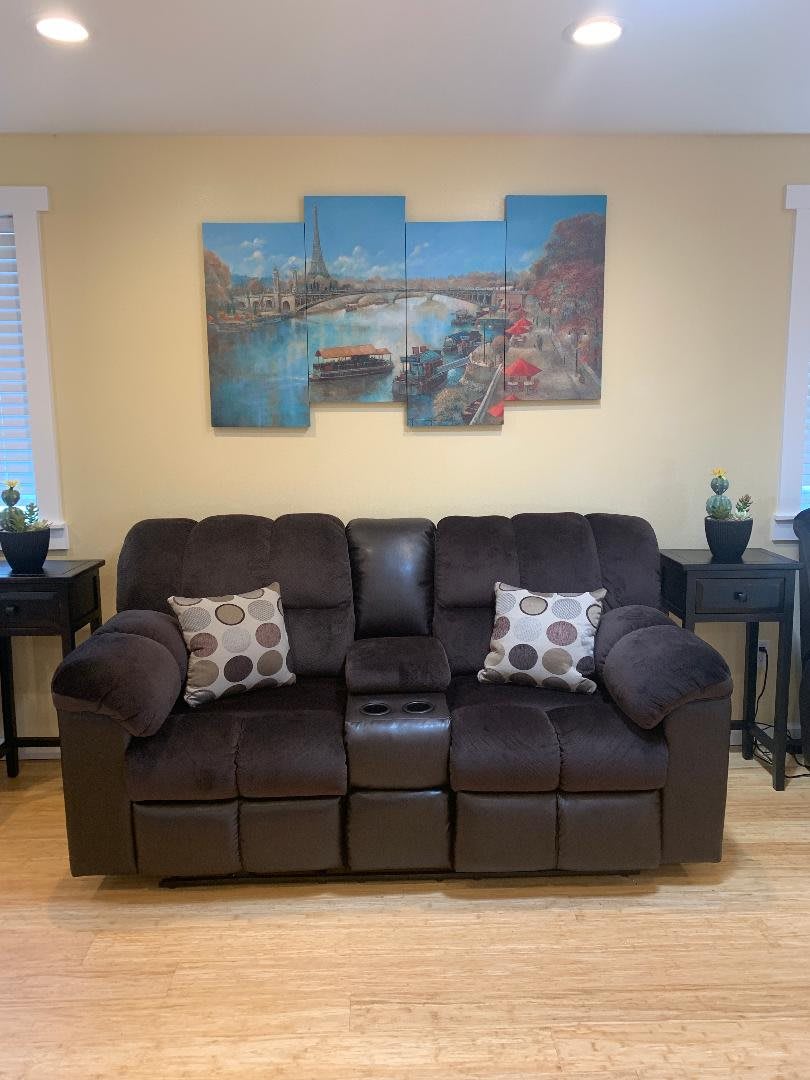 A cozy living room setup featuring a dark brown sofa with patterned pillows and a multi-panel artwork on the wall.