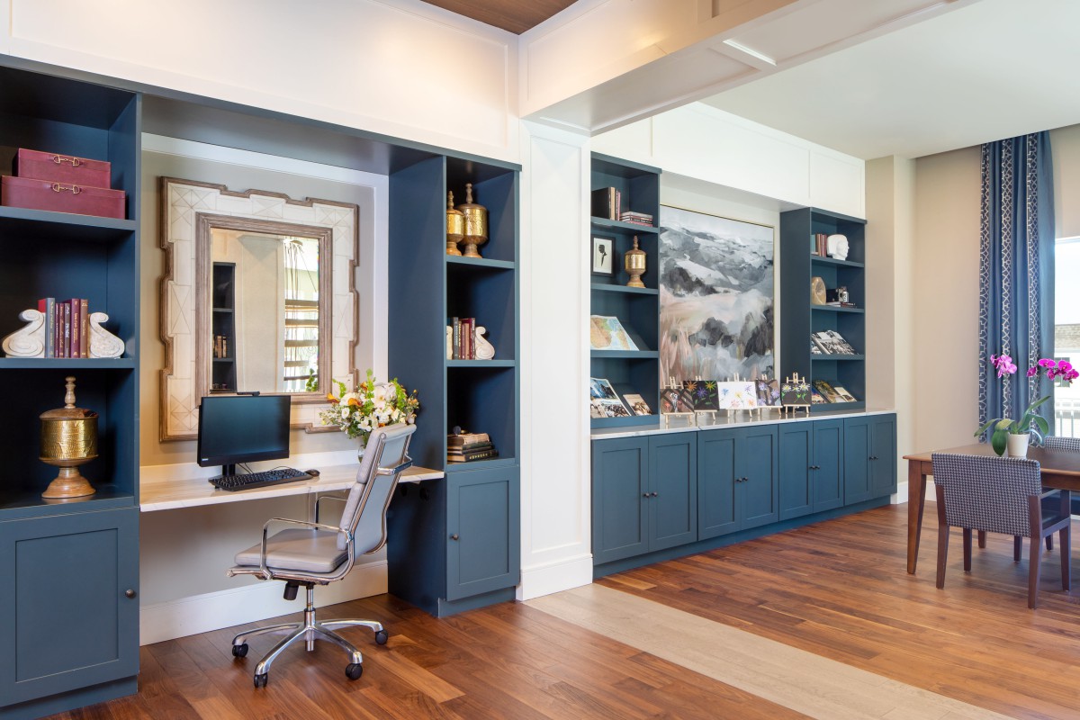 A modern home office with built-in blue bookshelves, a desk with a computer, and elegant decor.
