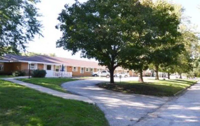 A peaceful neighborhood scene with a tree-lined sidewalk and buildings in the background.