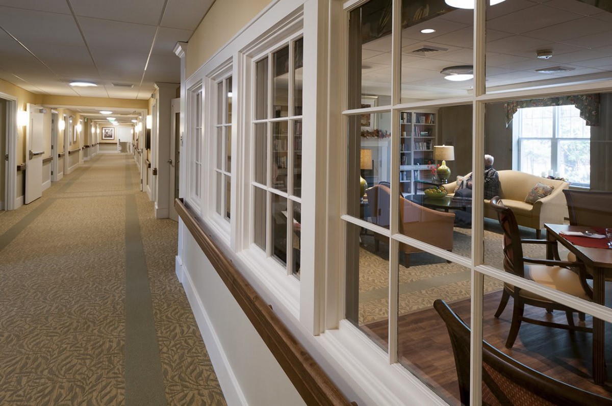 A well-lit interior hallway with large windows looking into a cozy room.