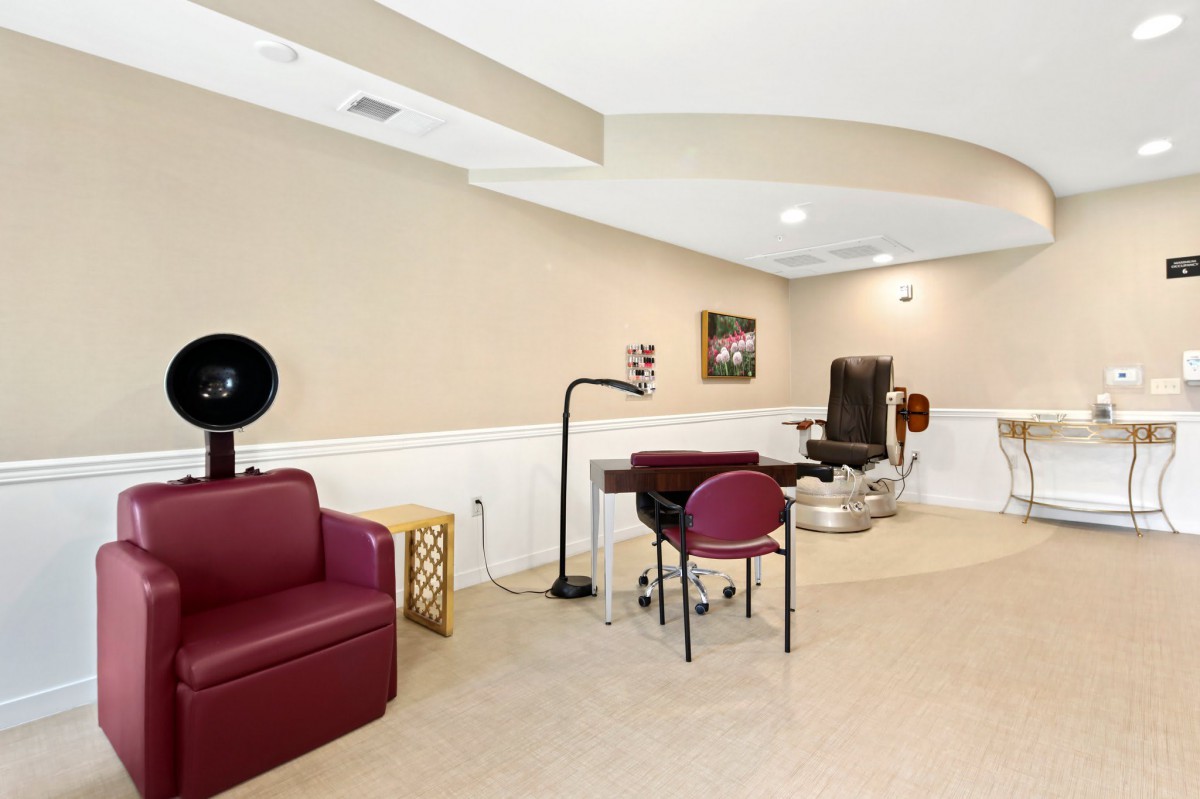 A beauty salon interior featuring a styling chair, table with lamp, and a sofa.