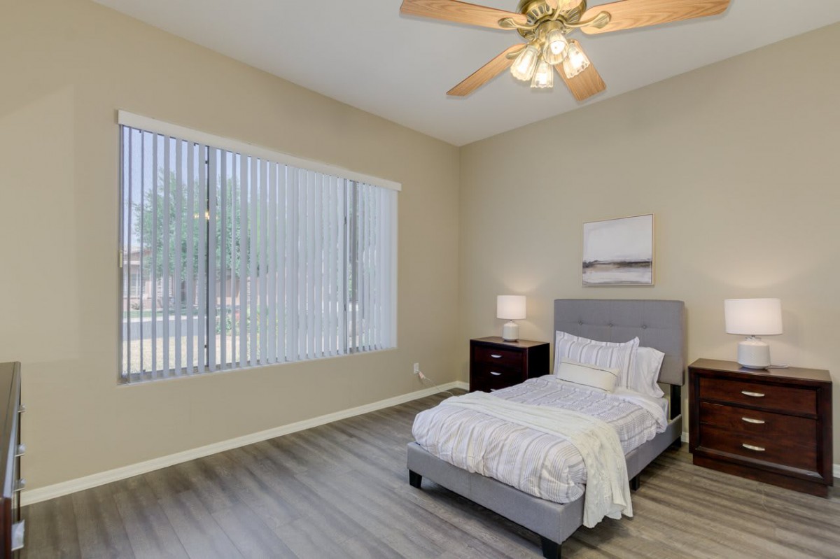 A minimalist bedroom with a single bed, nightstand, and a large window with blinds.