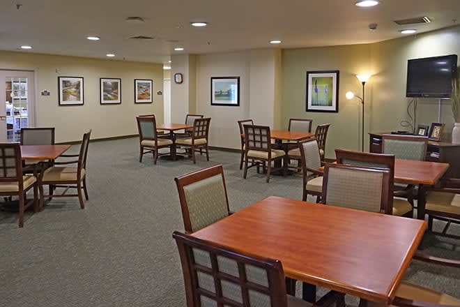 A spacious dining area with multiple tables and chairs, decorated with wall art and softly lit by lamps.