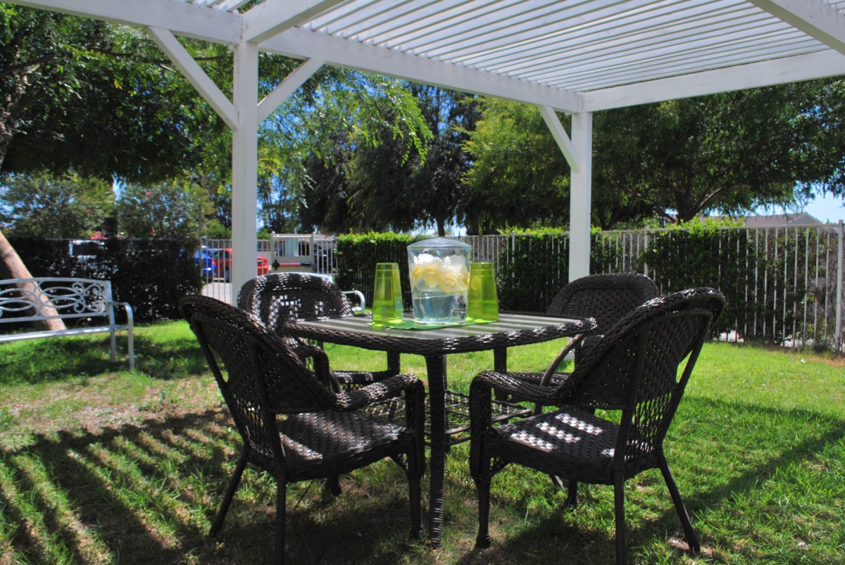 A cozy outdoor patio setup with a table and chairs under a pergola, featuring a refreshing pitcher of lemonade.
