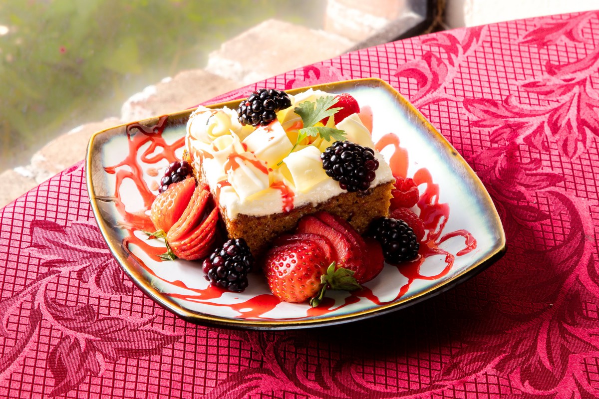 A delicious fruit-topped cake garnished with strawberries and blackberries on a decorative plate.