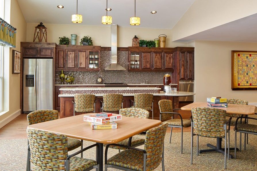 A modern kitchen interior with wooden cabinets, a countertop with bar stools, and a seating area with a table and chairs.