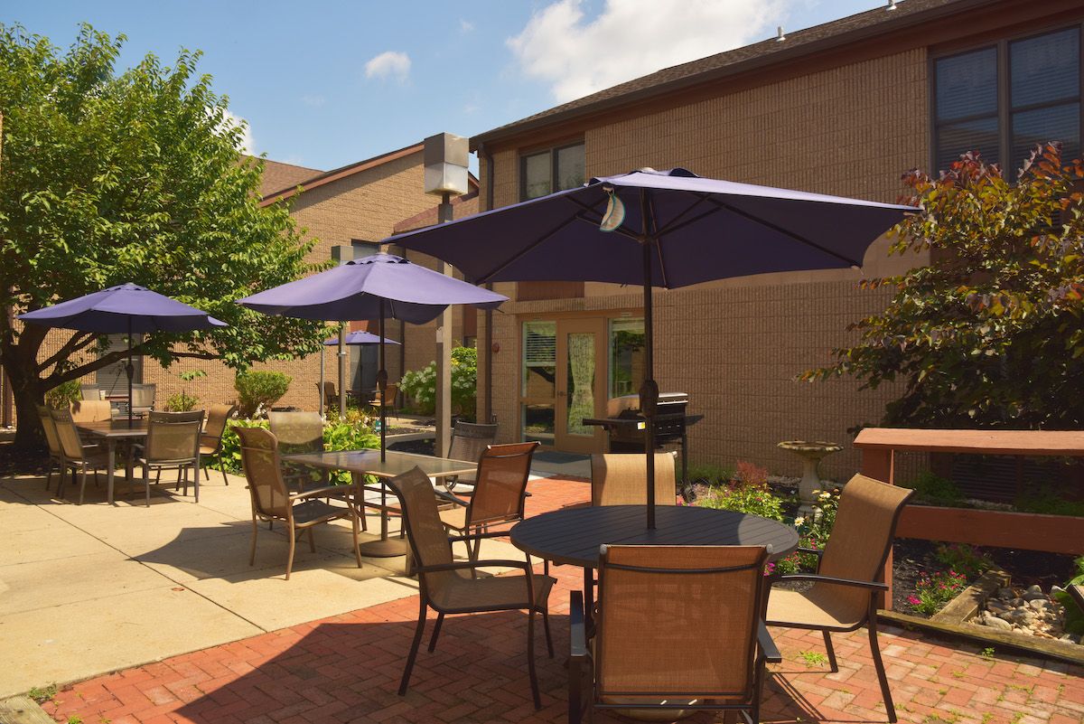 A sunny outdoor patio area with tables, chairs, and large umbrellas near a brick building.