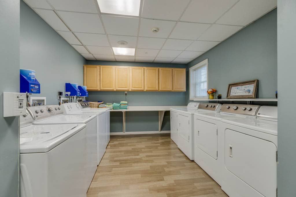 A clean and organized laundry room featuring multiple washers and dryers with overhead wooden cabinets and a folding counter.