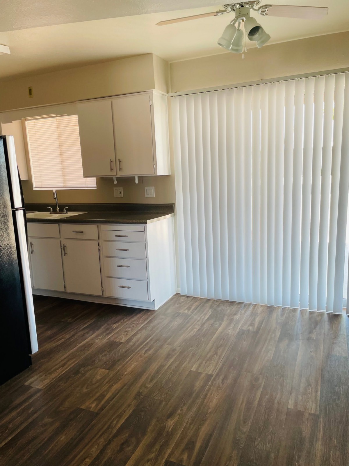 A modern apartment kitchen with wood flooring, white cabinets, and a refrigerator.