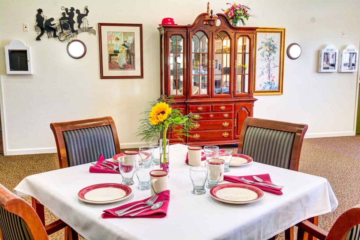 A well-set dining table with a flower centerpiece and a china cabinet in the background.