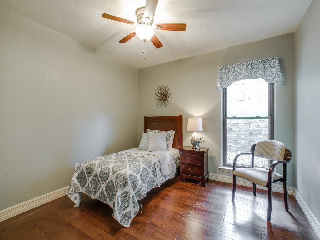 A cozy bedroom with a single bed, wooden flooring, and a ceiling fan.