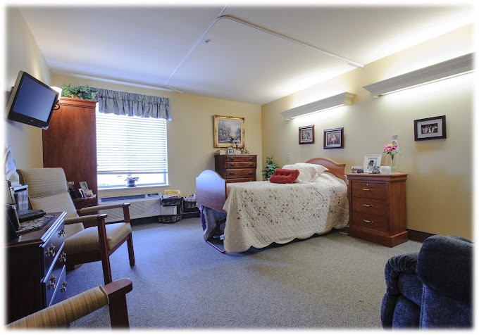 A cozy bedroom with a bed, dresser, and chairs near a window.