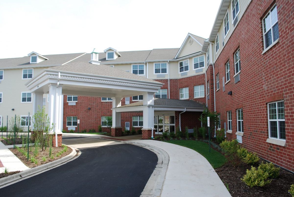 A view of a large residential building with a covered entrance and landscaped surroundings.