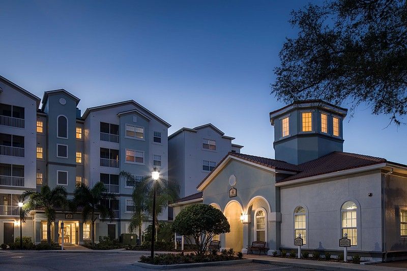 A serene evening view of a residential building complex with illuminated windows and surrounding trees.