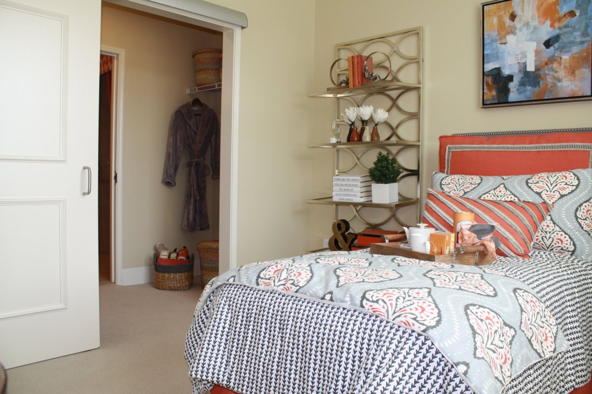 A cozy bedroom featuring a neatly made bed, an organized shelf with decor items, and an open closet displaying a hanging robe.