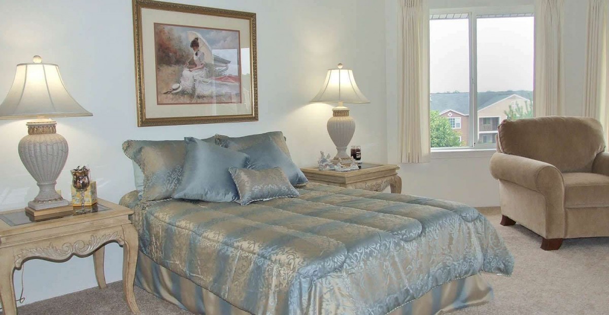 A cozy bedroom with a neatly made bed, decorative pillows, and a bedside lamp.