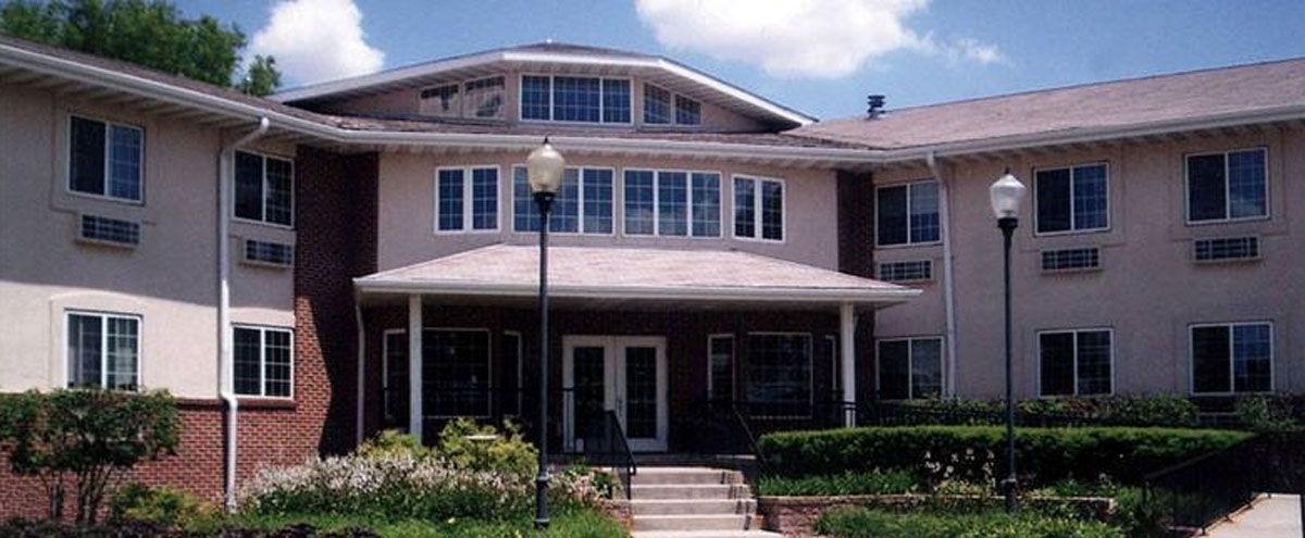 A two-story residential building with a porch, large windows, and a garden in front.