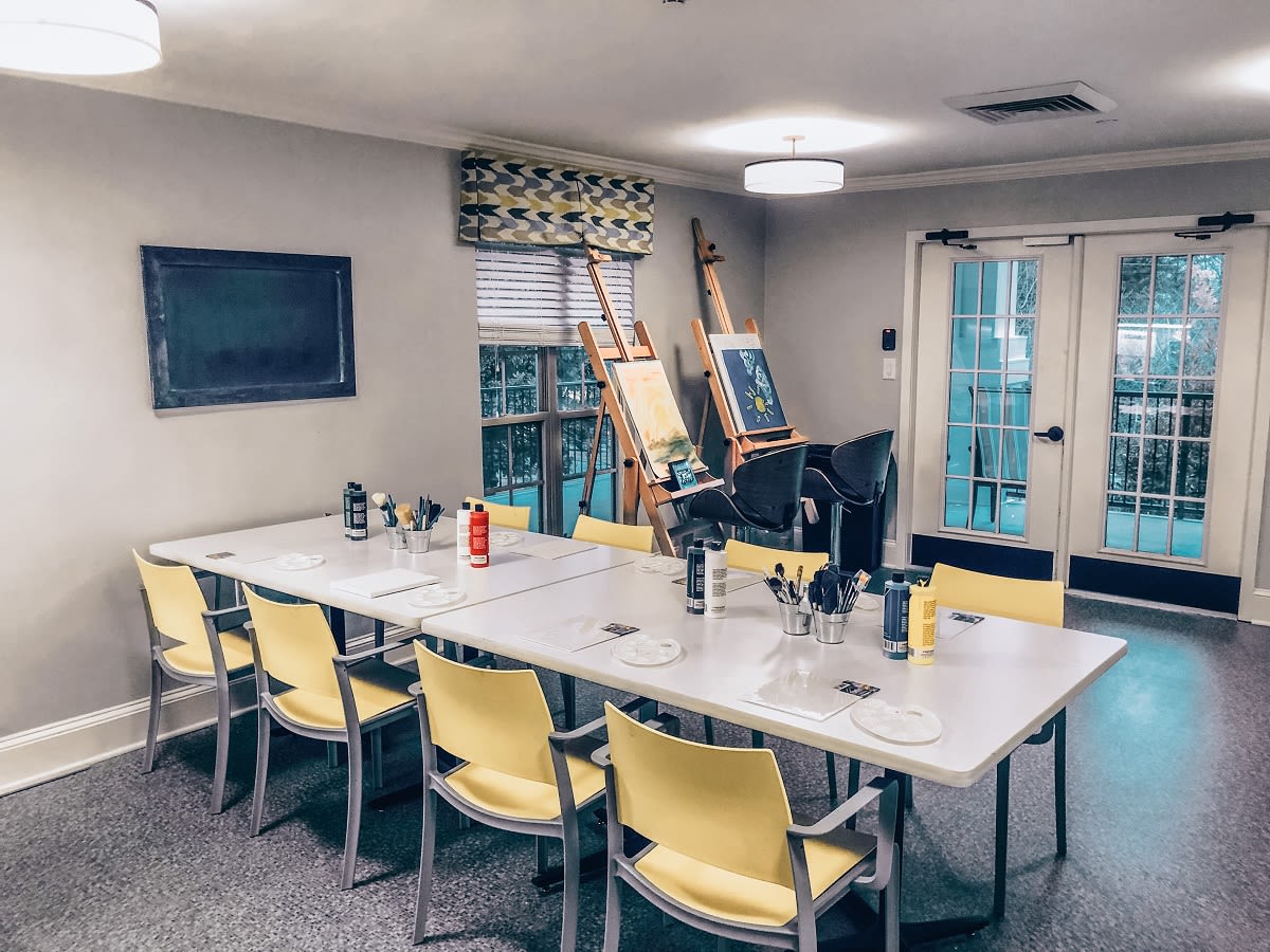 A creative workspace featuring a large table, yellow chairs, and easels set up for art projects.