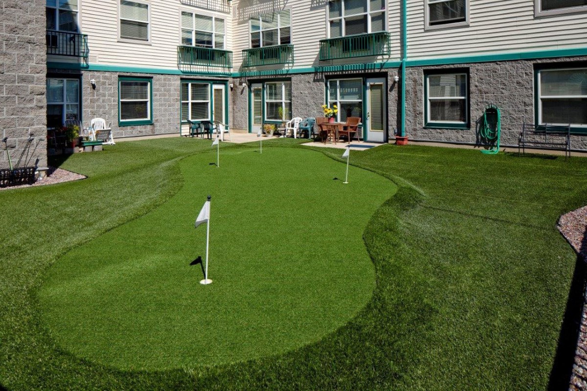 A small putting green set up in the backyard of a residential building with artificial turf and flags.