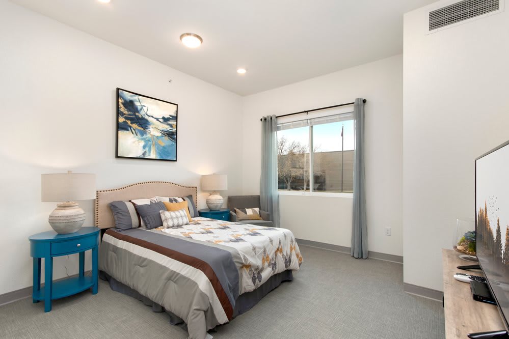 A modern bedroom interior with a bed, artwork, and natural light from a window.
