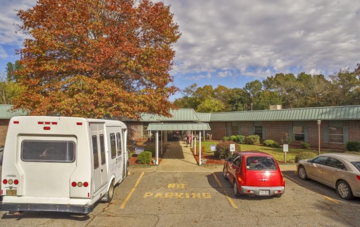 A small building with a parking lot in front, surrounded by autumn trees and a cloudy sky.