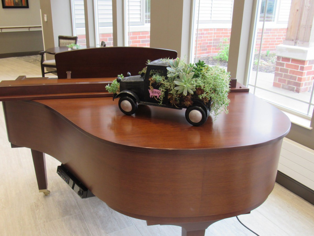 A decorative toy truck with plants sits atop a grand piano in a well-lit room.