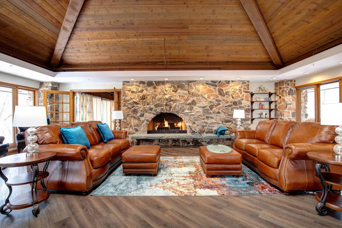 A cozy living room featuring leather couches, a stone fireplace, and wooden ceiling beams.