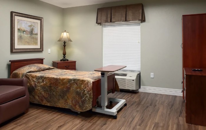 A hospital room with a bed, nightstand, and lamp.