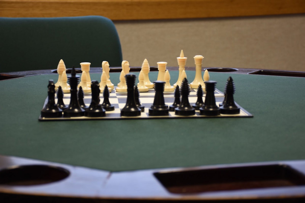 A chess board with pieces set up for a game on a green table.