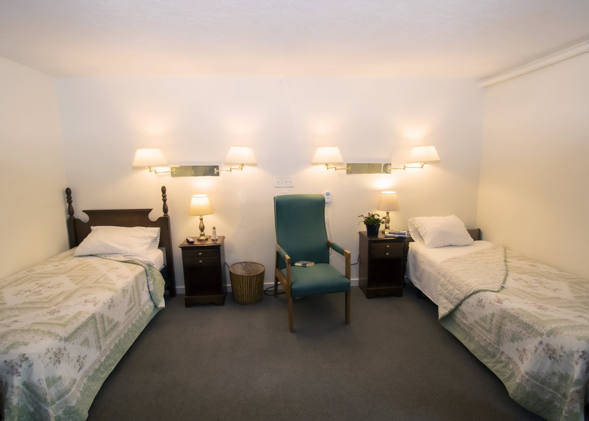 A cozy bedroom with two single beds, nightstands, and a chair in the center.