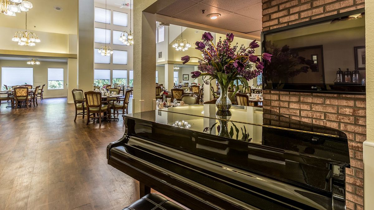 A cozy dining and music area featuring a grand piano and floral centerpiece, bathed in natural light.