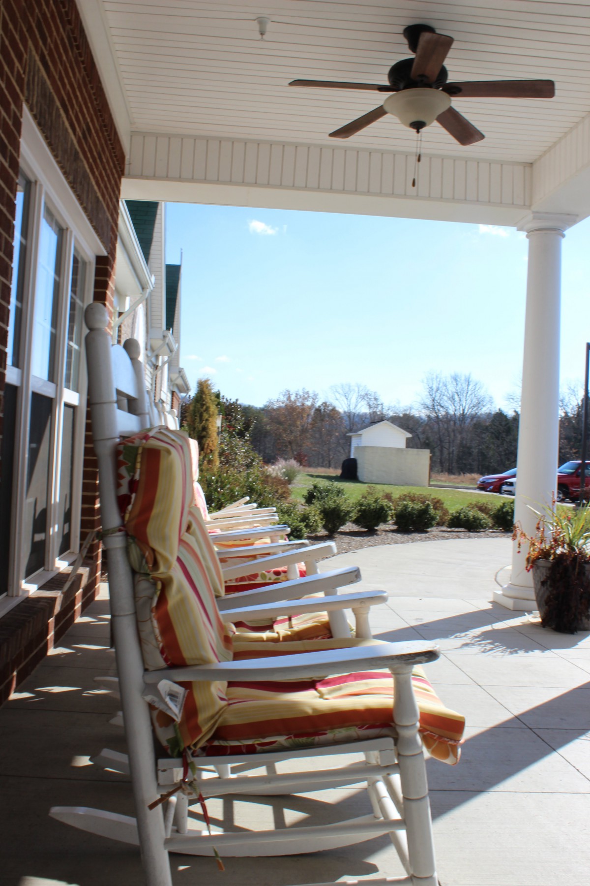 A row of rocking chairs on a sunny porch overlooking a garden.