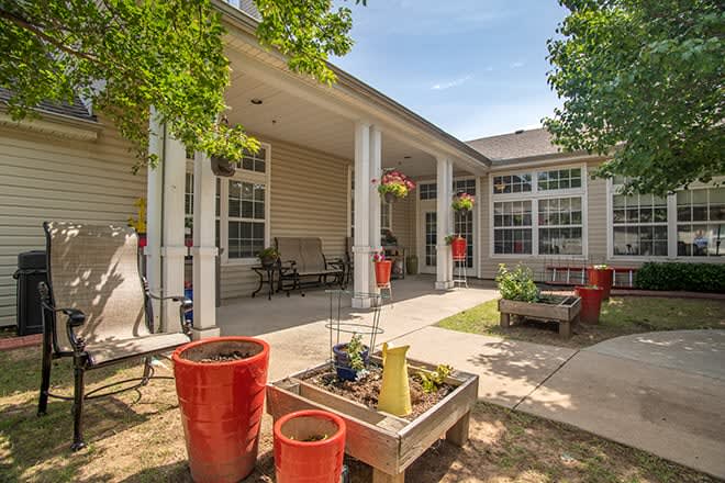 A cozy patio area with potted plants, benches, and hanging baskets under a clear blue sky.