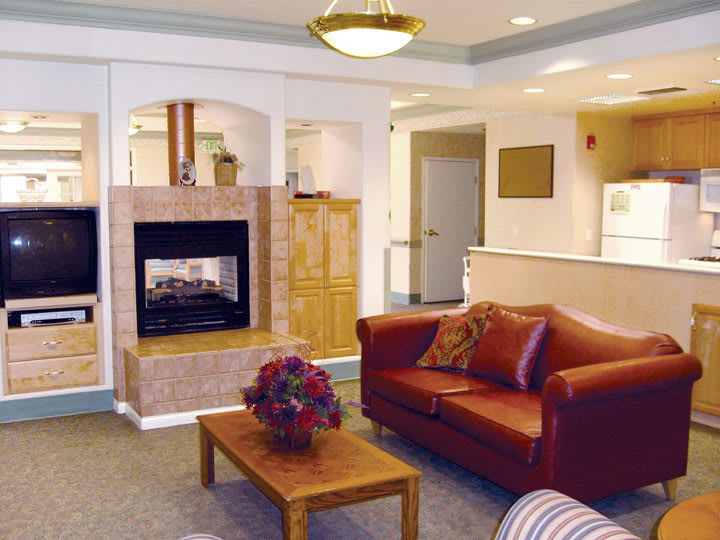 A cozy living room featuring a leather sofa, central fireplace, and a wooden coffee table with floral centerpiece.