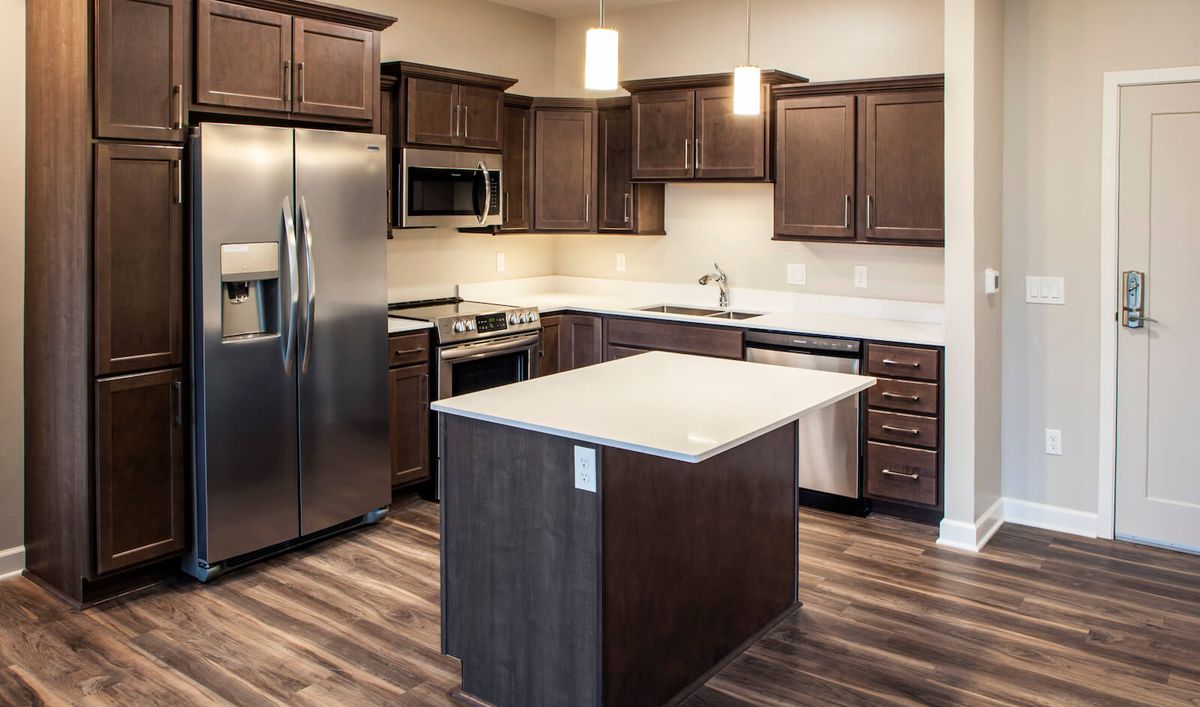 A modern kitchen featuring stainless steel appliances, wooden cabinets, and a central island with pendant lighting.