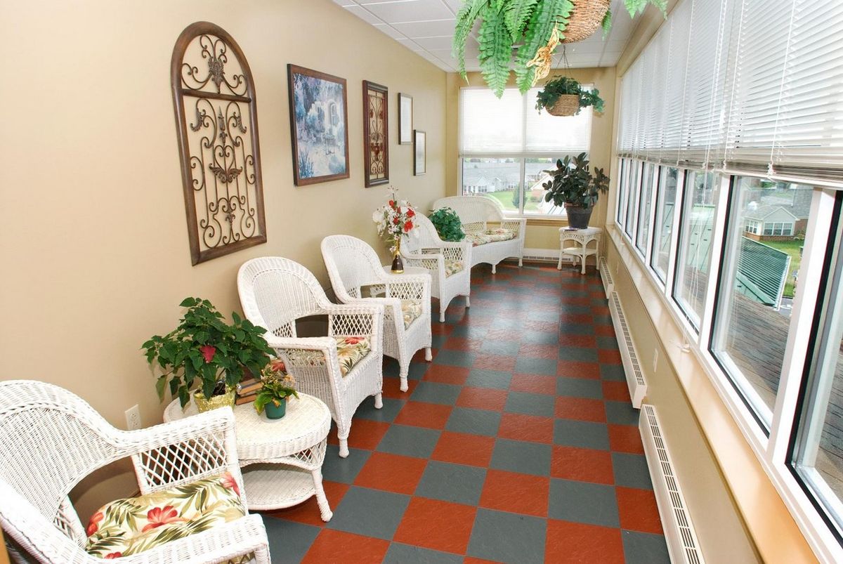 A bright and welcoming interior waiting area with wicker chairs, tables, and plants near large windows.