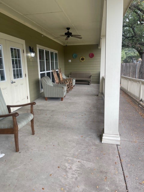A spacious outdoor porch with seating and a ceiling fan.