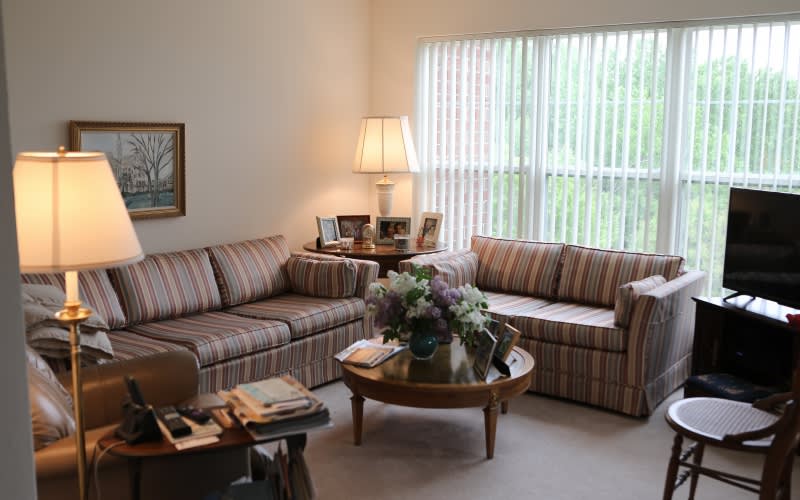 Cozy living room with striped sofas, a coffee table adorned with flowers, and a softly lit lamp by the window.
