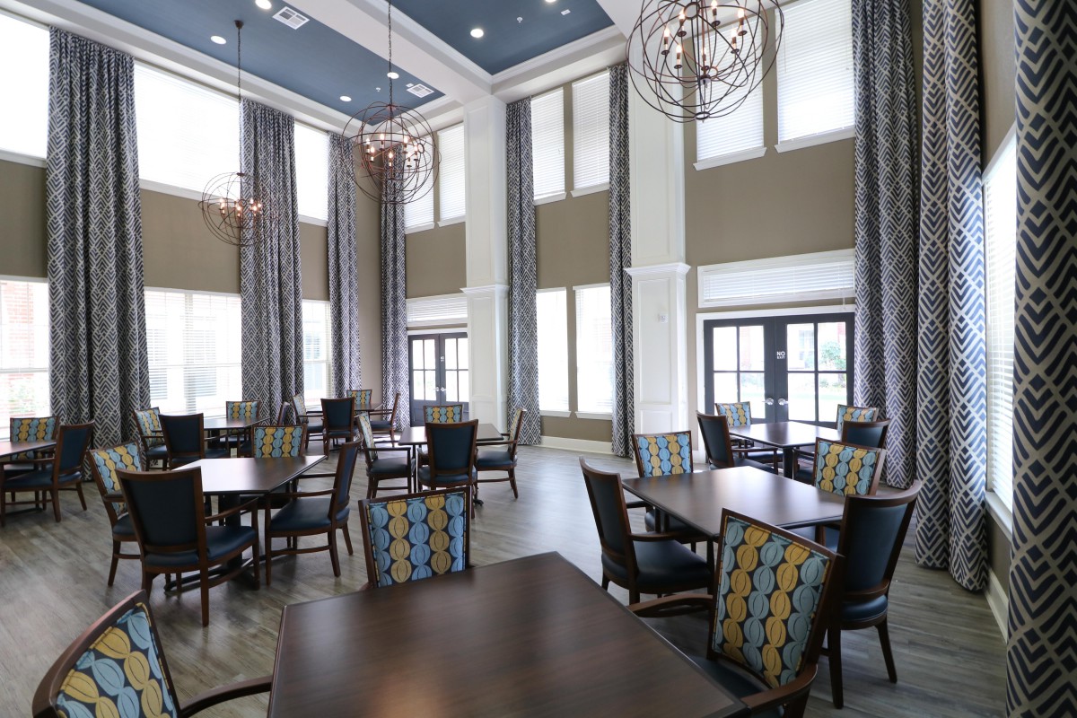 A modern dining room with high ceilings and large windows, featuring elegant chandeliers and stylish furniture.