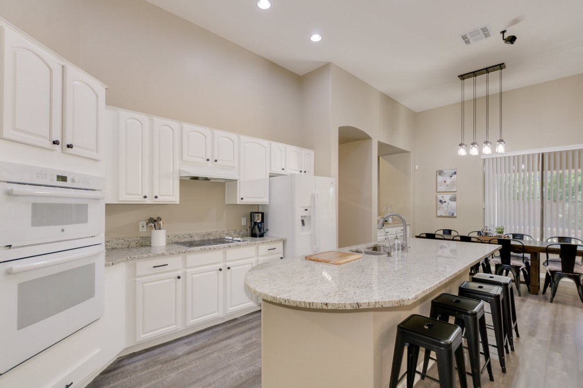 A modern kitchen with white cabinets, a large island, and bar stools.