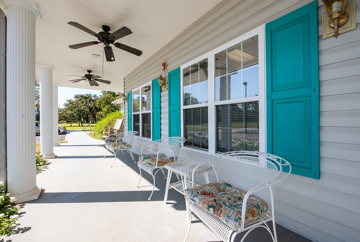 A sunny porch with blue shutters, equipped with chairs and ceiling fans.