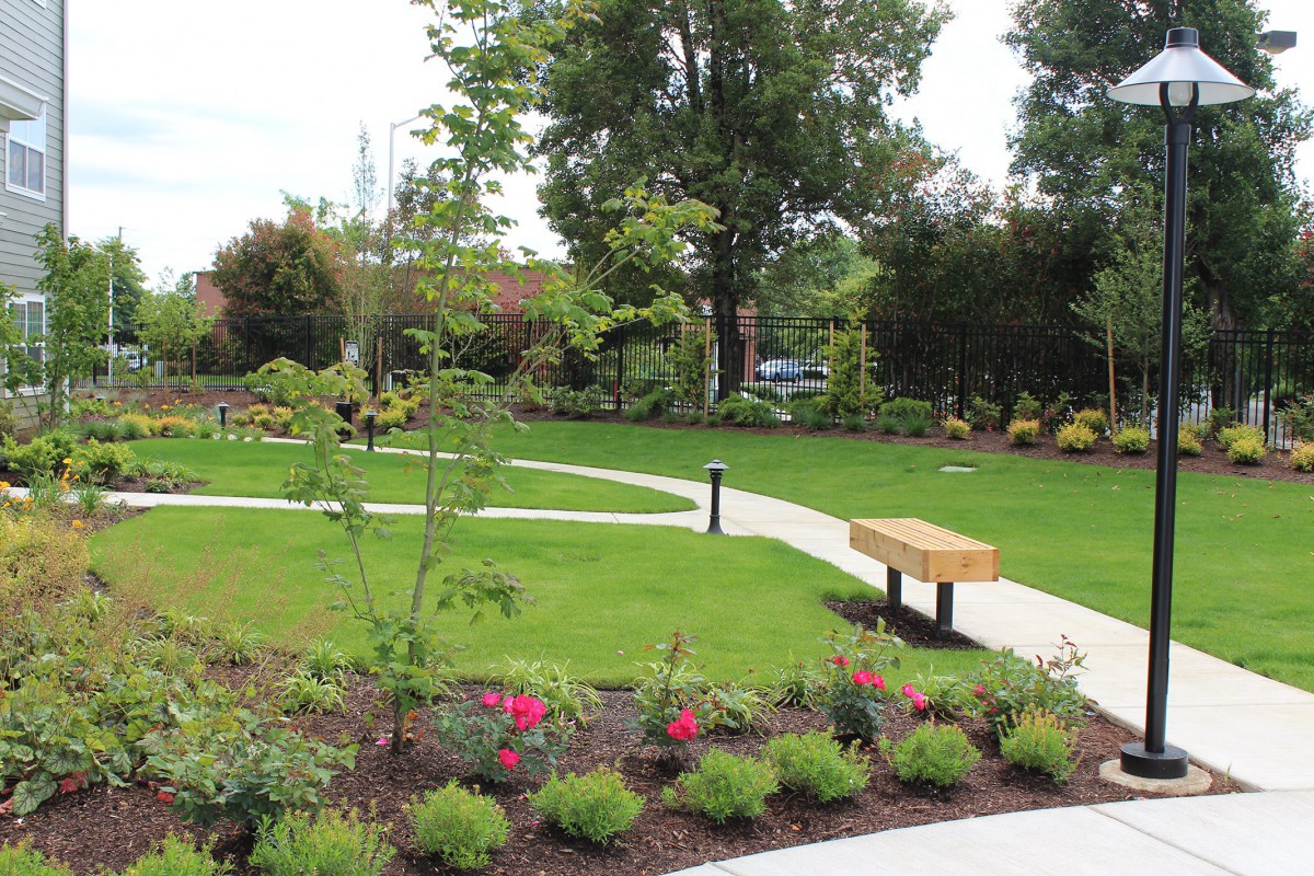 A beautifully landscaped garden with a pathway and benches surrounded by lush greenery and vibrant flowers.