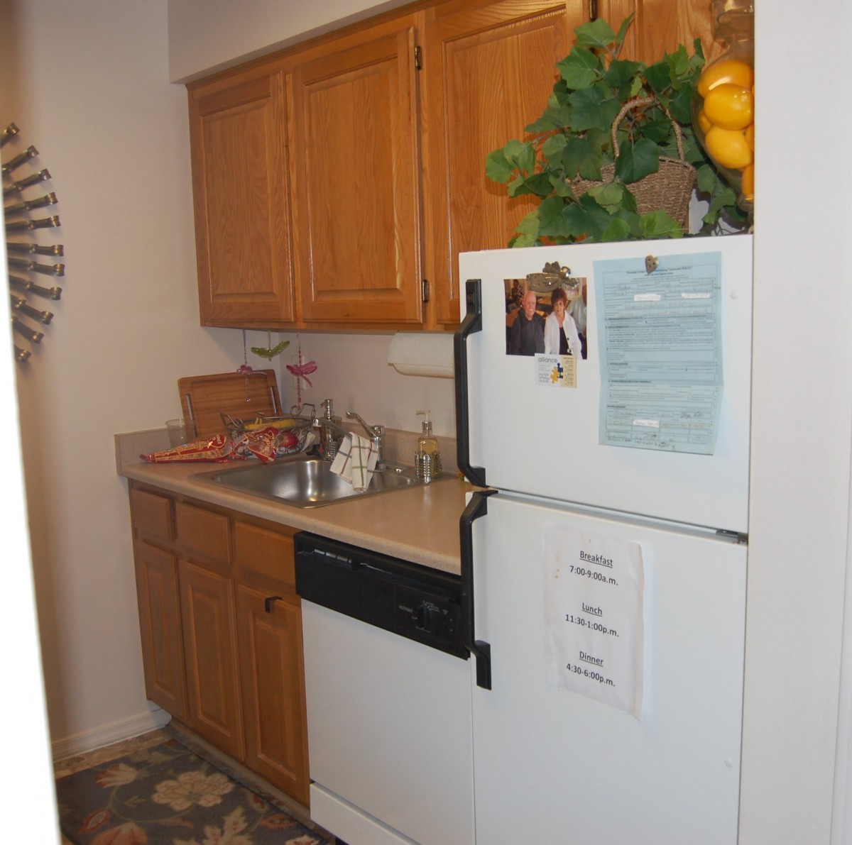 A cozy kitchen with wooden cabinets, a refrigerator adorned with notes, and a small counter space.